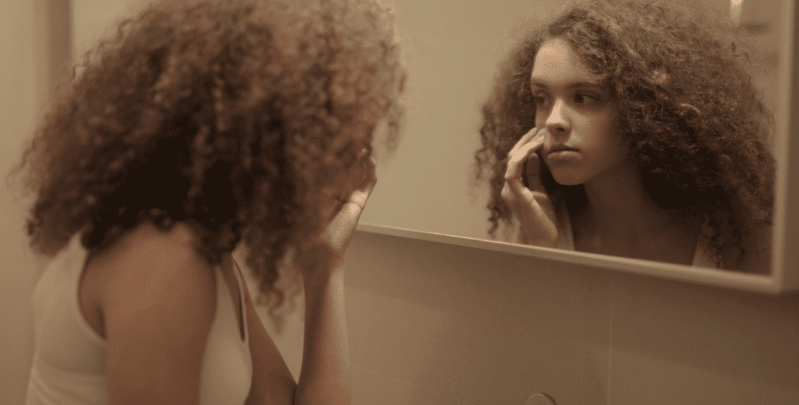 mulher analisando o rosto no espelho para identificar os tipos de pele
